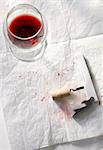 Half Empty Glass of Red Wine with Corkscrew and Wine Stains on Paper