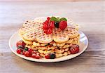 Waffles with raspberries, blueberries and redcurrants on a wooden plate