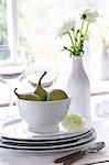 A stack of crockery with figs and a vase of white ranunculus flowers