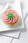 A cupcake topped with pink icing and a green flower
