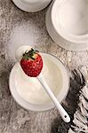Yoghurt on a spoon with a strawberry; a pot of sugar to one side