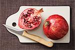 A whole and a half pomegranate on a chopping board with a knife