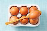 Brown eggs in a box and on a spoon (view from above)