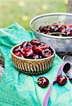 Fresh Cherries; A Bowl of Halved and Pitted Cherries and a Colander of Whole Fresh Ones