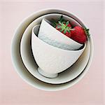 Two strawberries in white, overturned ceramic bowls