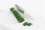 A bunch of chives and a knife on a chopping board