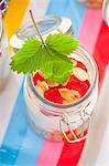 A jar containing ingredients for muesli: rolled oats, vanilla yoghurt and strawberries