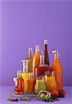 Freshly squeezed fruit juices in assorted glass containers against a purple background