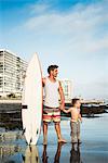 Young man holding surfboard with son in sea