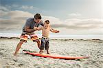 Young man teaching son to surf on beach