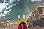 Legs and feet of skydiver above coastline