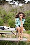 Young woman sitting on picnic table smiling, portrait