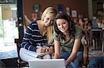 Two teenage girls using textbooks and computer in cafe