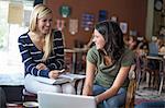 Two teenagers studying with textbooks and computer in cafe