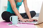 Young woman on yoga mat using laptop