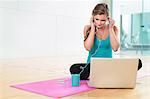 Young woman on yoga mat listening to smartphone