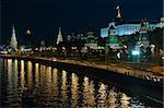 A night view of the Moscow city Kremlin with an illuminated river and a boat.