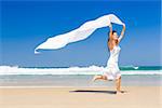 Beautiful woman running and jumping in the beach with a white tissue