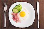 Fried egg with ham and cucumber on a plate