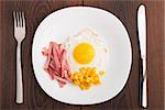 Fried egg with ham and corn on a white plate