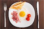 Fried egg with toasts, ham and cherry tomato on a plate