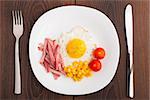 Fried egg with ham and vegetables on a white plate
