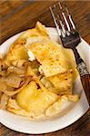 A plate of handmade pierogi with a side of caramelized onions.  There is a decorative silver and wood fork on the plate.  Everything is shot on a wood table.