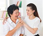 Sharing food. Happy Asian family sharing an ice cream at home. Beautiful senior mother and adult daughter eating dessert together.