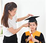 Asian child graduation, teacher adjusting cap for student indoor.