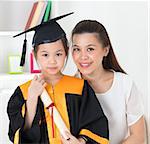 Asian school kid graduate in graduation gown and cap. Taking photo with mother.
