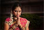 Portrait of beautiful young Indian woman in traditional sari dress praying in a hindu temple.