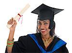 Happy Indian adult student in graduation gown and cap holding diploma certificate. Portrait of mixed race Asian Indian and African American female model standing isolated on white background.