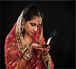 Beautiful young Indian woman in traditional sari dress holding a diwali oil lamp light, isolated on black background.