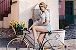 fashion portrait of sexy blonde woman with denim shorts sitting on bicycle with some coloured tulips in the basket