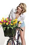 portrait of smiling blonde woman on bicycle wearing denim shorts posing near coloured tulips in the bikeâ??s basket  and showing her neckline