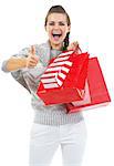 Surprised young woman in sweater with shopping bags showing thumbs up