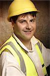 Confident builder, handyman or construction worker wearing hard hat and vest is smiling.