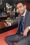 Cheerful businessman sending a text while having a drink in a classy bar