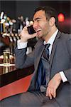 Cheerful businessman on the phone having a drink in a classy bar