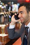 Smiling businessman on the phone having a drink in a classy bar