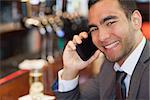 Happy handsome businessman on the phone having a drink in a classy bar