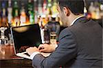 Handsome businessman working on his laptop while having a drink in a classy bar