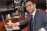 Smiling businessman working on his laptop in a classy bar