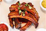 Close up of barbecue pork ribs served with salsa and mustard garnished with green onions