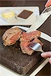 Medium rare steak sizzling on hot stone plate being sliced served in classy restaurant