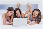 Friends lying on bed with laptop and laughing