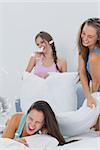 Laughing friends having pillow fight in bed at slumber party at home