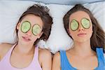 Friends lying in bed with cucumber slices on eyes at sleepover