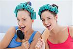 Friends in hair rollers singing into their hairbrushes at home at girls night in