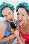 Friends in hair rollers holding hairbrush having fun and singing at sleepover